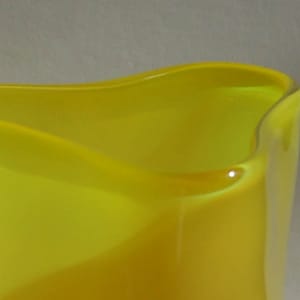 Puede incluir: Un jarrón de vidrio amarillo con un diseño ondulado único. El jarrón está hecho de vidrio transparente con un tinte amarillo.