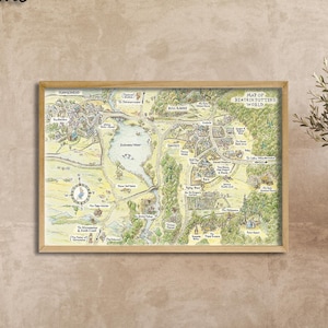 May include: A framed map of a fantasy world, with the text "Oak Frame" in the upper left corner. The map is in a light wood frame and features a detailed illustration of a landscape with a lake, buildings, and roads. The map is hanging on a beige wall.