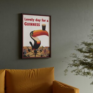 May include: Framed wall art featuring a toucan with a Guinness pint on its beak. The artwork has a vintage aesthetic with the text "Lovely day for a Guinness" in red. The toucan is perched on a weather vane, set against a cream background.