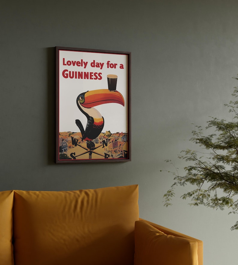 May include: Framed wall art featuring a toucan with a Guinness pint on its beak. The artwork has a vintage aesthetic with the text "Lovely day for a Guinness" in red. The toucan is perched on a weather vane, set against a cream background.