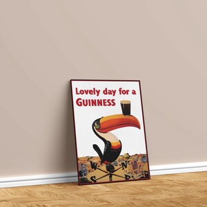 May include: Framed poster with a vintage Guinness advertisement. The artwork features a toucan with a large orange beak holding a pint of Guinness. Text reads "Lovely day for a Guinness."