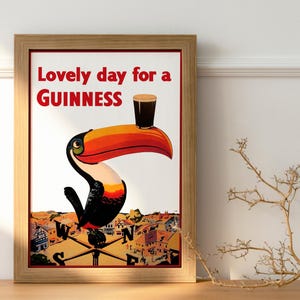 May include: Framed vintage-style Guinness advertisement. The artwork features a toucan balancing a pint of Guinness on its beak. The text at the top reads "Lovely day for a Guinness". The poster is in a wooden frame.