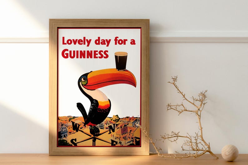 May include: Framed vintage-style Guinness advertisement. The artwork features a toucan balancing a pint of Guinness on its beak. The text at the top reads "Lovely day for a Guinness". The poster is in a wooden frame.