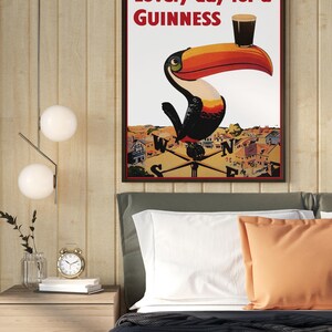 May include: Framed Guinness advertisement featuring a toucan with a pint of stout on its beak. The poster reads "Lovely day for a Guinness" in red text. The artwork is set against a backdrop of a town and a compass.