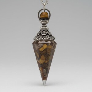 May include: A silver-toned pendulum with a clear, cone-shaped body filled with golden-brown stones. The pendulum has a decorative silver top and a small, faceted stone at the top, suspended from a chain.