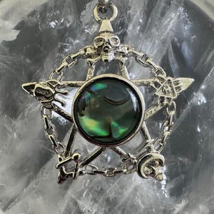May include: Silver-toned pendant featuring a pentagram design with a central iridescent stone. The pentagram is adorned with skulls, chains, and various symbols. The pendant is suspended from a matching chain, creating a gothic or occult aesthetic.