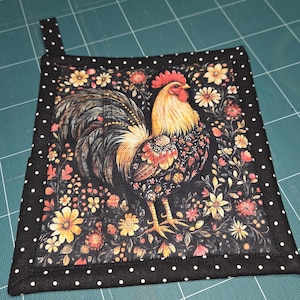May include: Square black and white polka dot pot holder with a rooster design. The rooster is in the center, surrounded by flowers in shades of yellow, orange, and pink. The rooster has a red comb and wattle.
