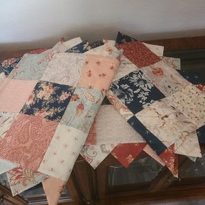 May include: A patchwork quilt with a variety of floral and paisley patterns in shades of pink, blue, and red. The quilt is made of rectangular and triangular fabric pieces, creating a decorative design. The quilt is folded over a wooden cabinet.