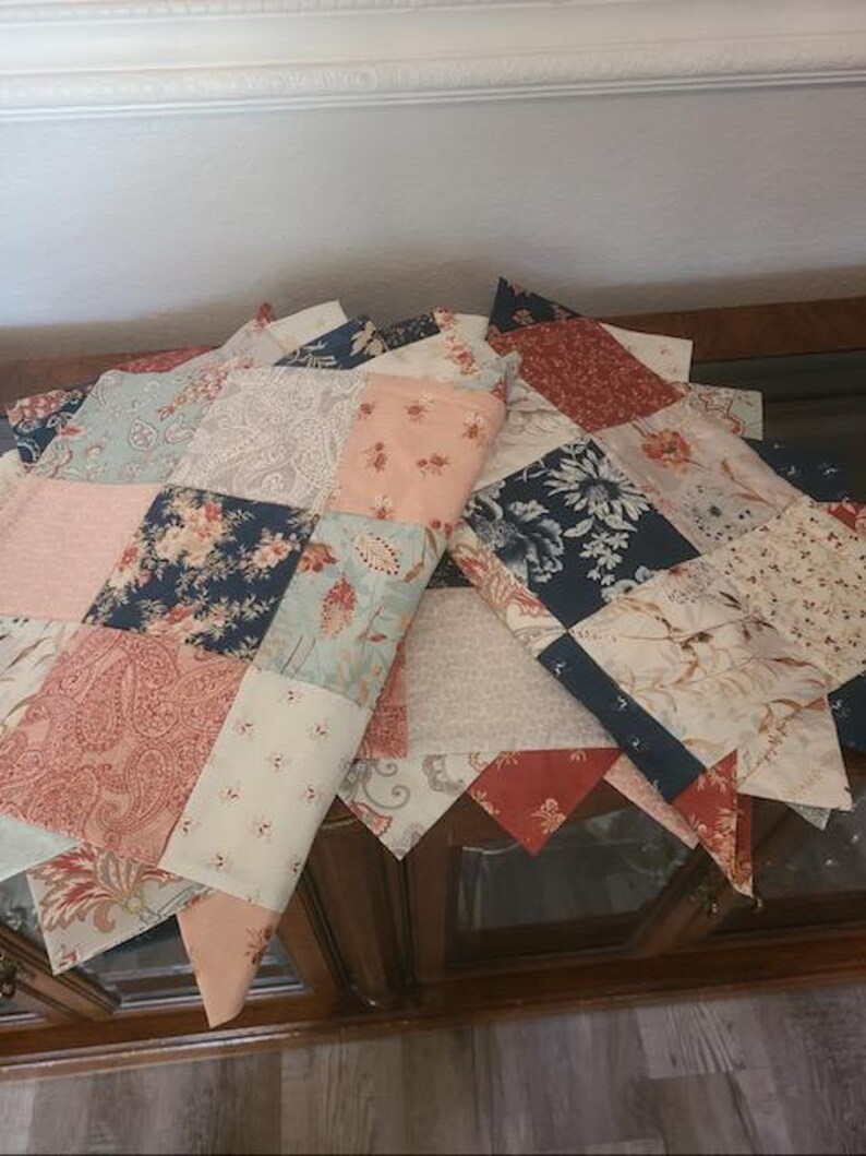 May include: A patchwork quilt with a variety of floral and paisley patterns in shades of pink, blue, and red. The quilt is made of rectangular and triangular fabric pieces, creating a decorative design. The quilt is folded over a wooden cabinet.