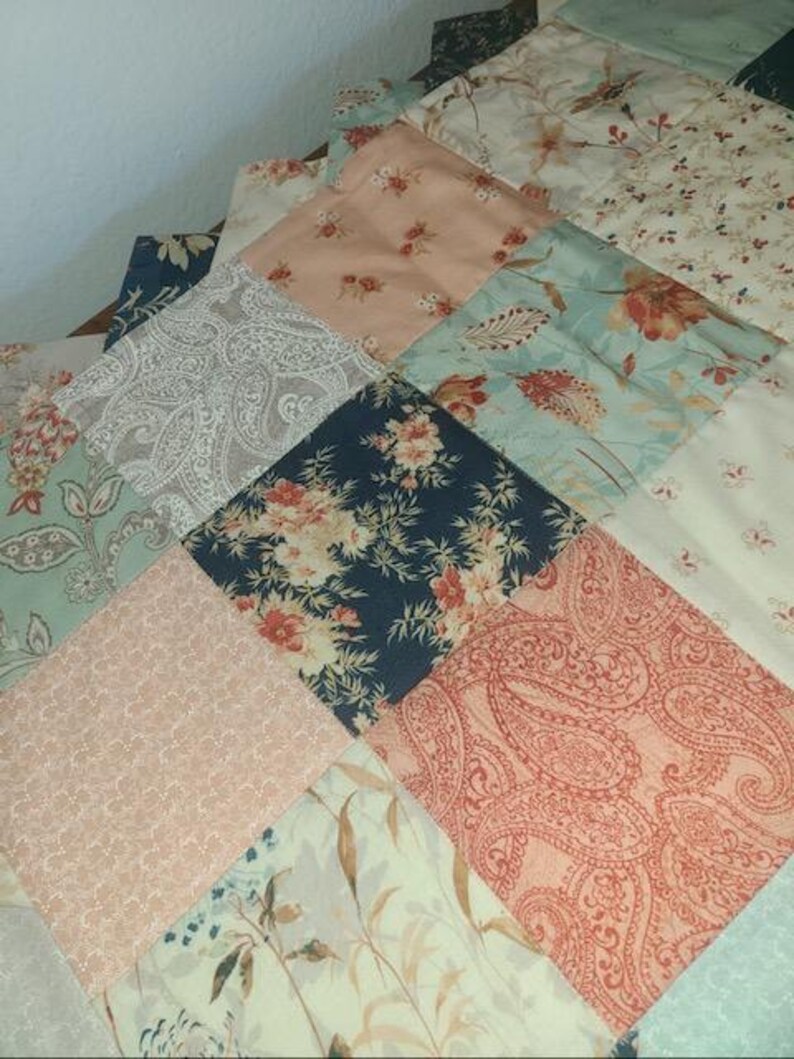 May include: A patchwork quilt with a variety of floral and paisley patterns in shades of blue, peach, and cream. The quilt is made of square fabric pieces sewn together, creating a textured surface.