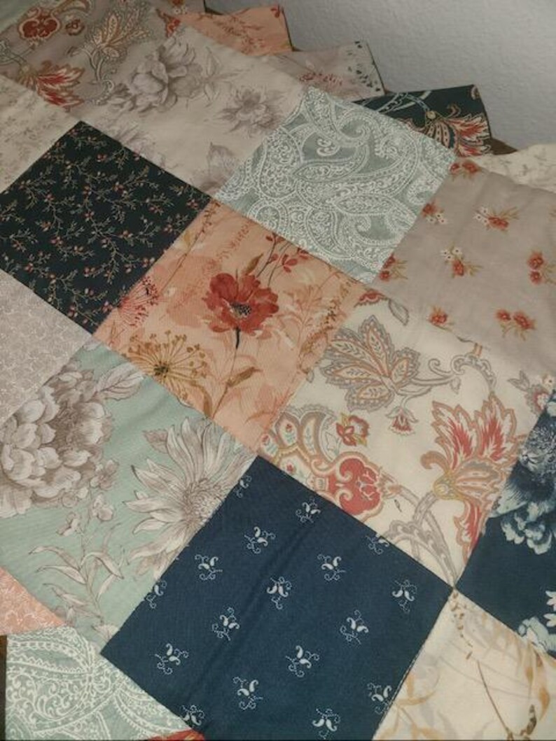 May include: A patchwork quilt featuring a variety of floral and paisley patterns in shades of pink, green, blue, and beige. The quilt is made of square fabric pieces sewn together, creating a textured surface. The overall design is a mix of vintage and modern styles.
