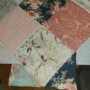 May include: A patchwork quilt with various floral and paisley patterns in shades of pink, teal, navy, and cream. The quilt is made of diamond-shaped fabric pieces, creating a geometric design. The fabrics feature detailed botanical and ornamental motifs.