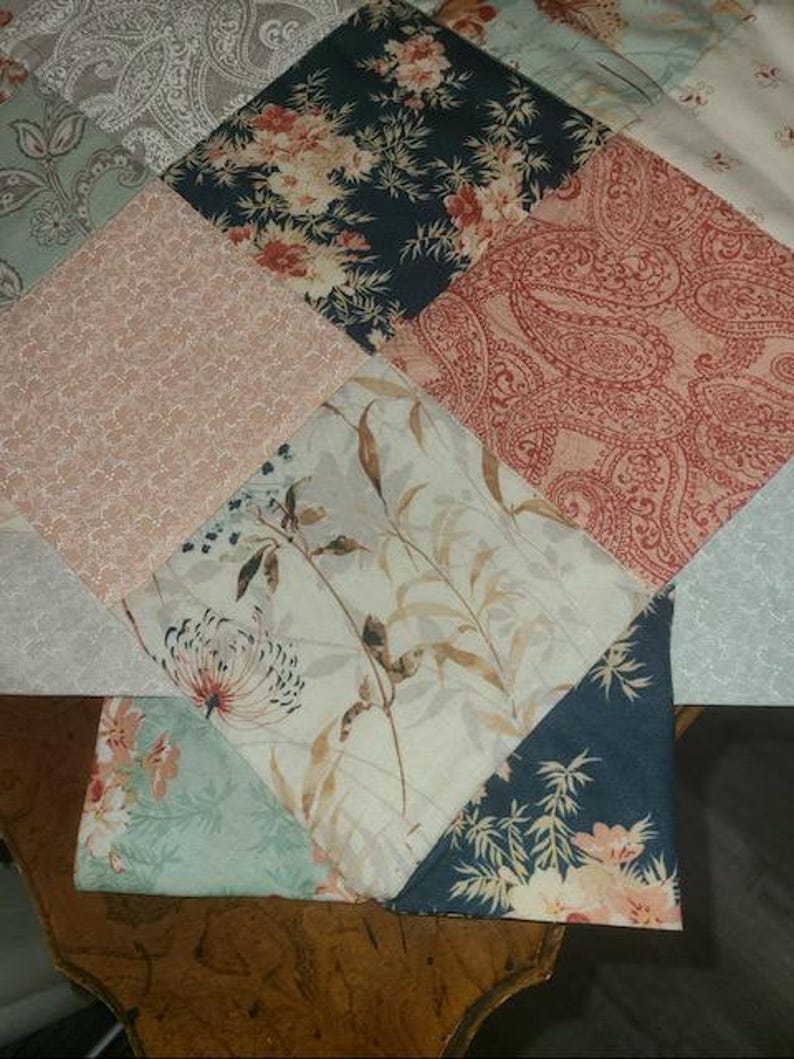 May include: A patchwork quilt with various floral and paisley patterns in shades of pink, teal, navy, and cream. The quilt is made of diamond-shaped fabric pieces, creating a geometric design. The fabrics feature detailed botanical and ornamental motifs.