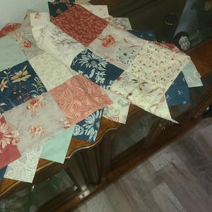May include: A patchwork quilt with a variety of floral and paisley patterns in shades of red, blue, cream, and green. The quilt is made of multiple fabric squares sewn together, creating a decorative textile.