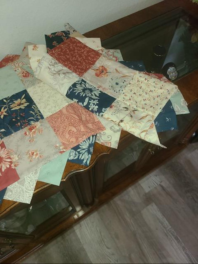 May include: A patchwork quilt with a variety of floral and paisley patterns in shades of red, blue, cream, and green. The quilt is made of multiple fabric squares sewn together, creating a decorative textile.