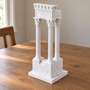 May include: A white architectural model of a classical temple structure featuring three fluted Corinthian columns, a rectangular base with brick-like detailing, and a top frieze clearly inscribed with the text TITVLR in capital letters.