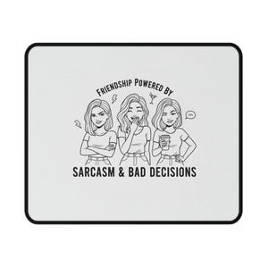 以下が含まれることがあります： 黒い縁取りのある白い長方形のマウスパッド。マウスパッドには、3人の女性の白黒イラストと「FRIENDSHIP POWERED BY SARCSM & BAD DECISIONS」というテキストが描かれています。
