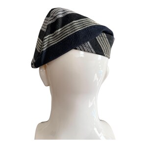 May include: A black and grey striped beret. The hat is made of a woven fabric with alternating black and grey stripes. The hat is displayed on a white mannequin head.