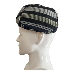 May include: A black and silver striped newsboy cap. The cap is made of a woven fabric with horizontal stripes. The cap is shown on a white mannequin head, viewed in profile.