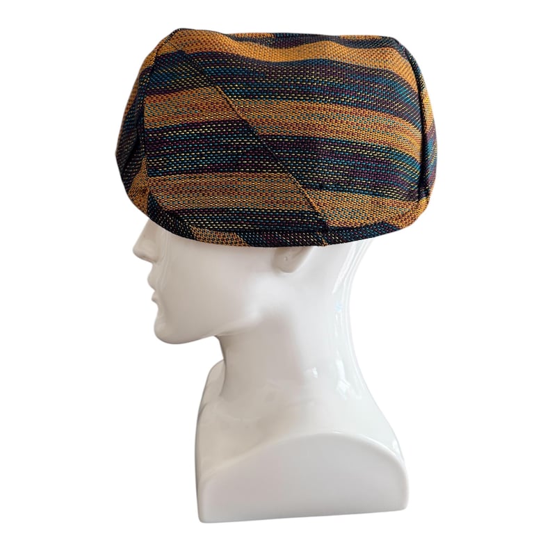 May include: A multi-colored, striped newsboy cap. The cap features horizontal stripes in shades of gold, teal, and dark blue. The cap is displayed on a white mannequin head. The cap is a stylish accessory.