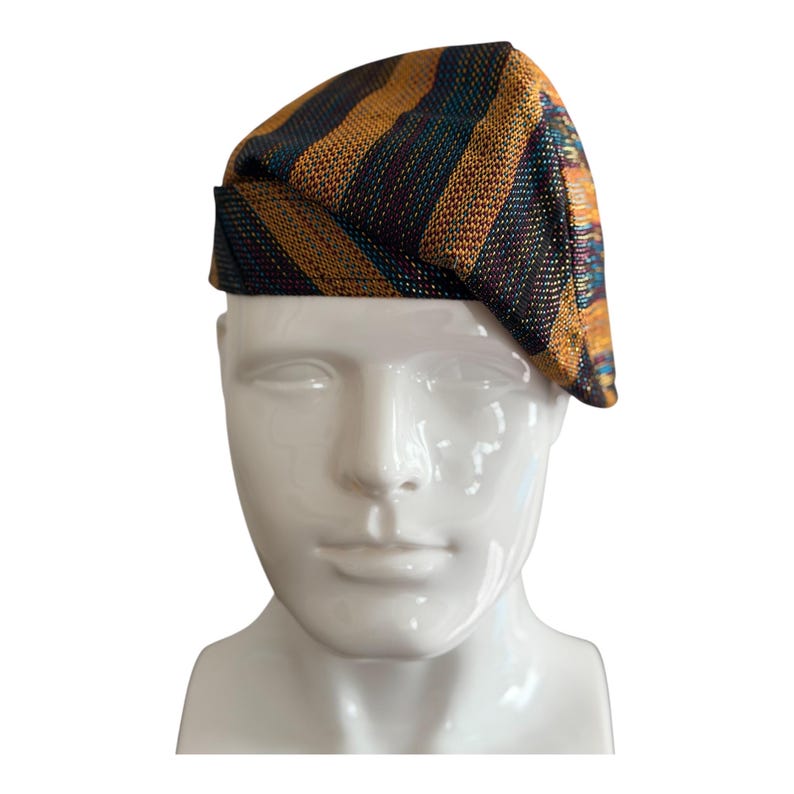 May include: A striped beret in shades of gold, teal, and dark brown. The beret is displayed on a white mannequin head. The fabric has a woven texture. This hat is a stylish accessory.