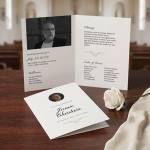 May include: A funeral service program, open to display the inside pages. The program is white with black text and a photo of a person. The program includes the obituary, order of service, and the date of the service.