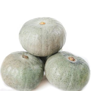 Puede incluir: Tres calabazas redondas de color verde pálido con sutiles motas grises y piel lisa y acanalada. Las calabazas están apiladas en forma de pirámide, cada una con un pequeño tallo leñoso de color marrón claro en el centro de su parte superior.
