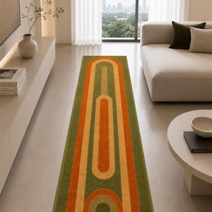 Può includere: Un lungo tappeto rettangolare dal design retrò. Il tappeto presenta strisce verticali nei toni del verde, arancione e beige. Il design include una serie di archi collegati. Il tappeto è collocato in un moderno soggiorno.