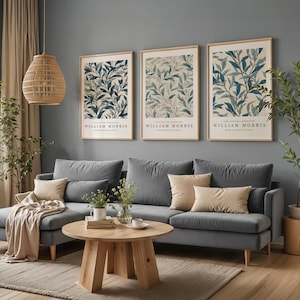 May include: Three framed botanical prints with blue and white leaf designs hang above a gray sofa with beige pillows. The prints are labeled "WILLIAM MORRIS." A round wooden coffee table and a woven pendant light complete the room's decor.
