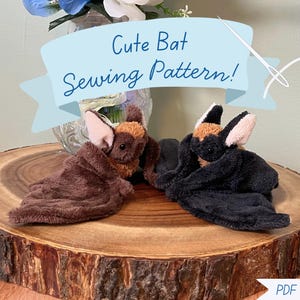 May include: Two plush bat toys, one brown and one black, featuring soft fabric, pointed ears with light pink inner sections, and dark eyes. A light blue banner across the top displays the text Cute Bat Sewing Pattern! and a PDF Download label.