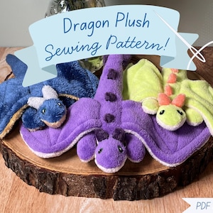 May include: Three plush dragon toys in blue, purple, and green, displayed on a wooden slice. The dragons have wings and detailed faces. The image includes text that reads "Dragon Plush Sewing Pattern!" and "PDF Download".