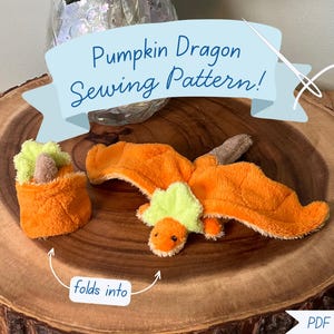 May include: A plush orange and lime green dragon toy that folds into a pumpkin shape. The image includes the text Pumpkin Dragon Sewing Pattern and folds into, indicating a PDF download for a craft project featuring this soft fabric creature.