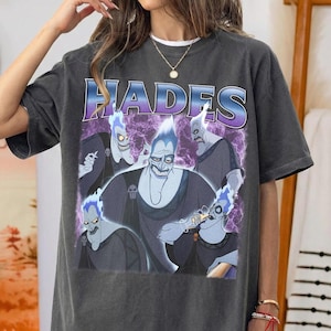 May include: Dark gray t-shirt featuring a graphic of Hades from Disney's Hercules. The word "HADES" is printed across the top in purple and blue. The graphic shows Hades with his blue flames and other characters.