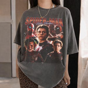 May include: Dark gray t-shirt featuring a graphic of Spider-Man and Peter Parker. The design includes multiple images of the character in his suit, with the text "SPIDER-MAN Peter Parker" in a vintage style.
