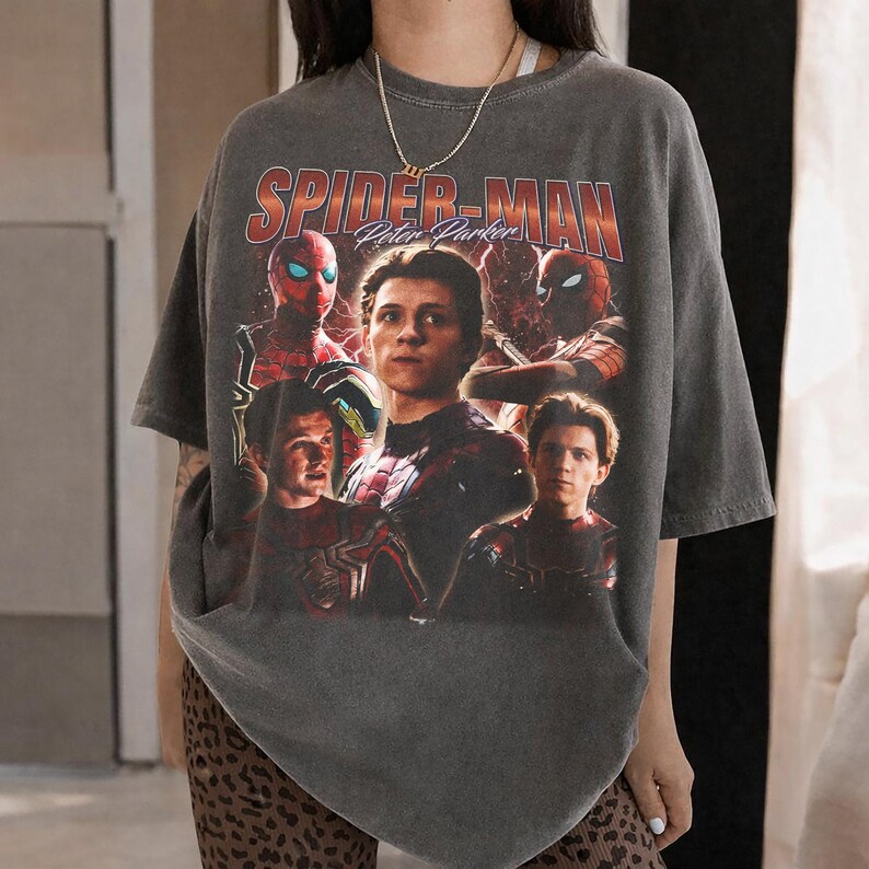 May include: Dark gray t-shirt featuring a graphic of Spider-Man and Peter Parker. The design includes multiple images of the character in his suit, with the text "SPIDER-MAN Peter Parker" in a vintage style.