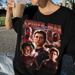 May include: Black t-shirt featuring a collage of images of Spider-Man and the text "Spider-Man Peter Parker" in red and orange. The shirt has a vintage, distressed look.