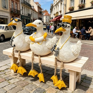 Könnte beinhalten: Drei skurrile Entenfiguren sitzen auf einer Holzbank. Jede Ente ist weiß mit gelben Schnäbeln und Füßen. Eine trägt eine Sonnenbrille und eine Ankerkette, eine andere eine Schwimmweste und die dritte eine Kapitänsmütze und ein Fernglas. Die Bank ist aus hellem Holz.