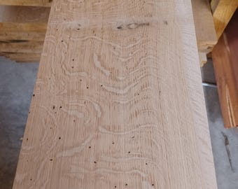 May include: Close-up of a light-colored, unfinished wooden plank with visible grain patterns and small knots. The wood has a natural, raw appearance, suggesting it's ready for use in woodworking projects. The plank is part of a larger stack of lumber.