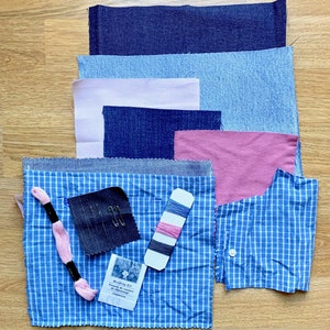 May include: A blue and white checkered fabric with a smaller blue fabric square, a pink thread, a small package of needles, a small package of thread, and a pink and blue thread. There is also a pink fabric square, a blue fabric square, and a light blue fabric square.
