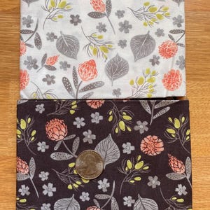 K&ouml;nnte beinhalten: Zwei Stoffquadrate mit floralen Mustern. Eines ist wei&szlig; mit grauen Bl&auml;ttern, korallenfarbenen Bl&uuml;ten und gelben Akzenten. Das andere ist dunkelbraun mit dem gleichen floralen Design. Eine M&uuml;nze liegt auf dem braunen Stoff zur Gr&ouml;&szlig;enbestimmung.