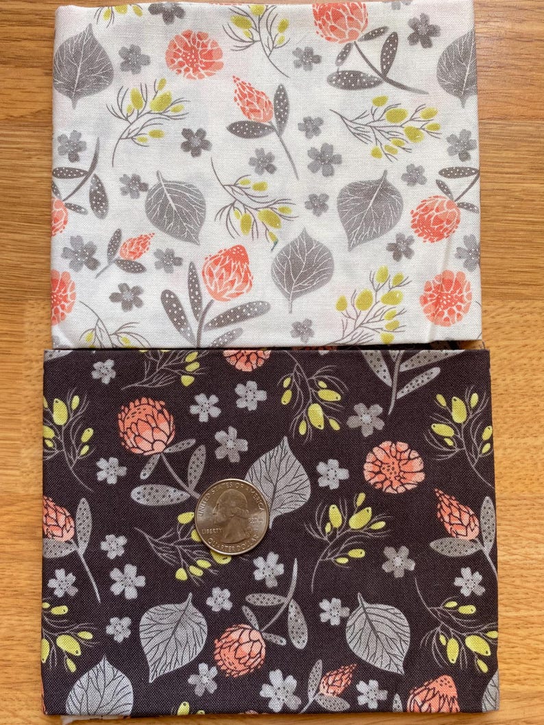 K&ouml;nnte beinhalten: Zwei Stoffquadrate mit floralen Mustern. Eines ist wei&szlig; mit grauen Bl&auml;ttern, korallenfarbenen Bl&uuml;ten und gelben Akzenten. Das andere ist dunkelbraun mit dem gleichen floralen Design. Eine M&uuml;nze liegt auf dem braunen Stoff zur Gr&ouml;&szlig;enbestimmung.