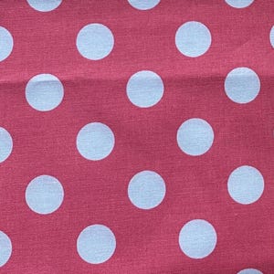 May include: Close-up of a fabric with a repeating pattern of large, light blue polka dots on a deep red background. The fabric has a slightly textured appearance.