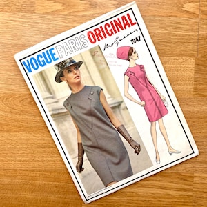 Puede incluir: Un patrón de costura vintage Vogue Paris Original de 1947. El patrón presenta dos vestidos, uno en gris y otro en rosa. El patrón se titula "Vogue Paris Original" e incluye el nombre del diseñador, "Molynoux".