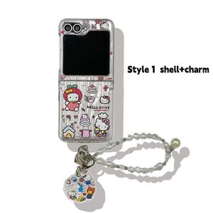 Peut inclure: Coque de t&eacute;l&eacute;phone transparente avec des graphismes Hello Kitty et un charm assorti. L'&eacute;tui pr&eacute;sente un design &agrave; rabat et comprend une dragonne perl&eacute;e. Le texte "Style 1 shell+charm" est visible.
