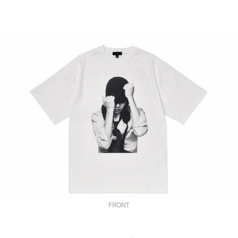 Puede incluir: Camiseta blanca de manga corta con un estampado gr&aacute;fico en blanco y negro. El gr&aacute;fico representa a una persona con las manos levantadas hacia la cabeza. La palabra "FRONT" est&aacute; impresa en la parte inferior de la camiseta.