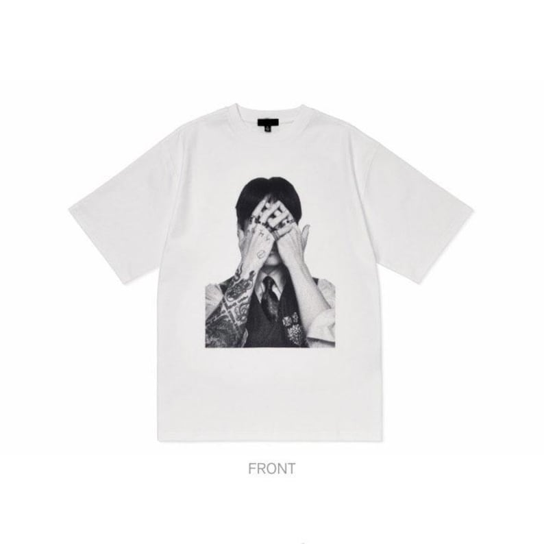 Puede incluir: Camiseta blanca de manga corta con un gr&aacute;fico en blanco y negro de una persona cubri&eacute;ndose los ojos. La persona lleva un chaleco y corbata. La palabra "FRONT" est&aacute; impresa en la parte inferior.