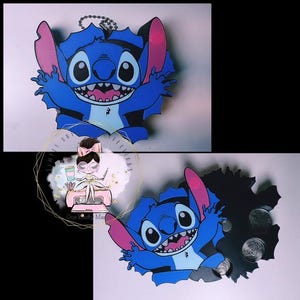 May include: A blue and black character-shaped keychain featuring a wide-eyed, smiling creature with large pink-lined ears. The design shows the character breaking through a dark background. A metal ball chain is attached to the top for hanging.