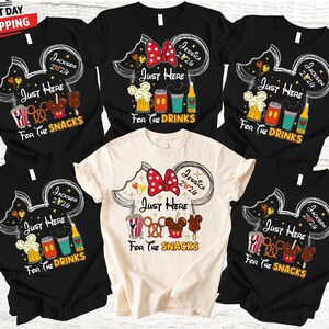 May include: A collection of black and cream-colored t-shirts featuring a Mickey Mouse head design. Each shirt has the text "Just Here For The Snacks" or "Just Here For The Drinks", along with other graphics and text.