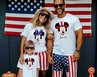 May include: Family wearing matching white t-shirts with Mickey and Minnie Mouse designs, and names. The family is standing in front of an American flag. The shirts are paired with red, white, and blue shorts and skirts. The image has a patriotic theme.