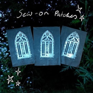 May include: Three black sew-on patches with a silver gothic window design and a cat silhouette at the bottom. The text "Sew-on Patches" is written in white script above the patches. Stars are drawn in white.